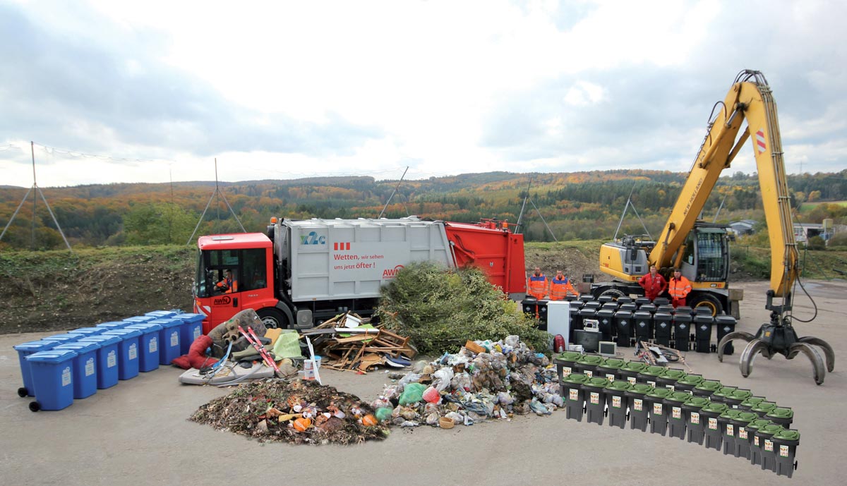 Beispielfoto (Montage) der Abfallmengen, die der neuen Standardgebühr von 203,95 € entsprechen  (von links): Altpapier, Sperrmüll, Bioabfall, Altholz, Grüngut, Restmüll (vorne), Elektronschrott, Altme-tall sowie die dazugehörigen Abfalltonnen entsprechend den jährlichen Leerungen (13 bzw. 26). 